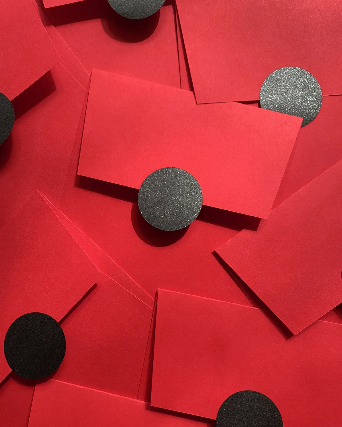 A scattered pile of vibrant red envelopes, each sealed with a round, textured black sticker.
