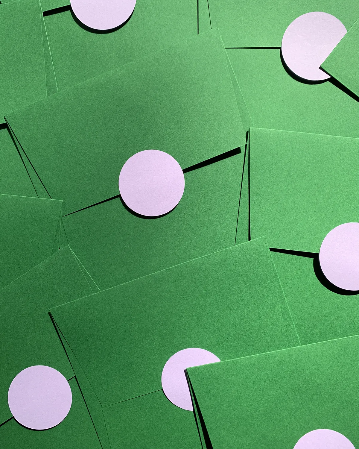 A scattered pile of green envelopes, each sealed with a round, light lilac sticker.