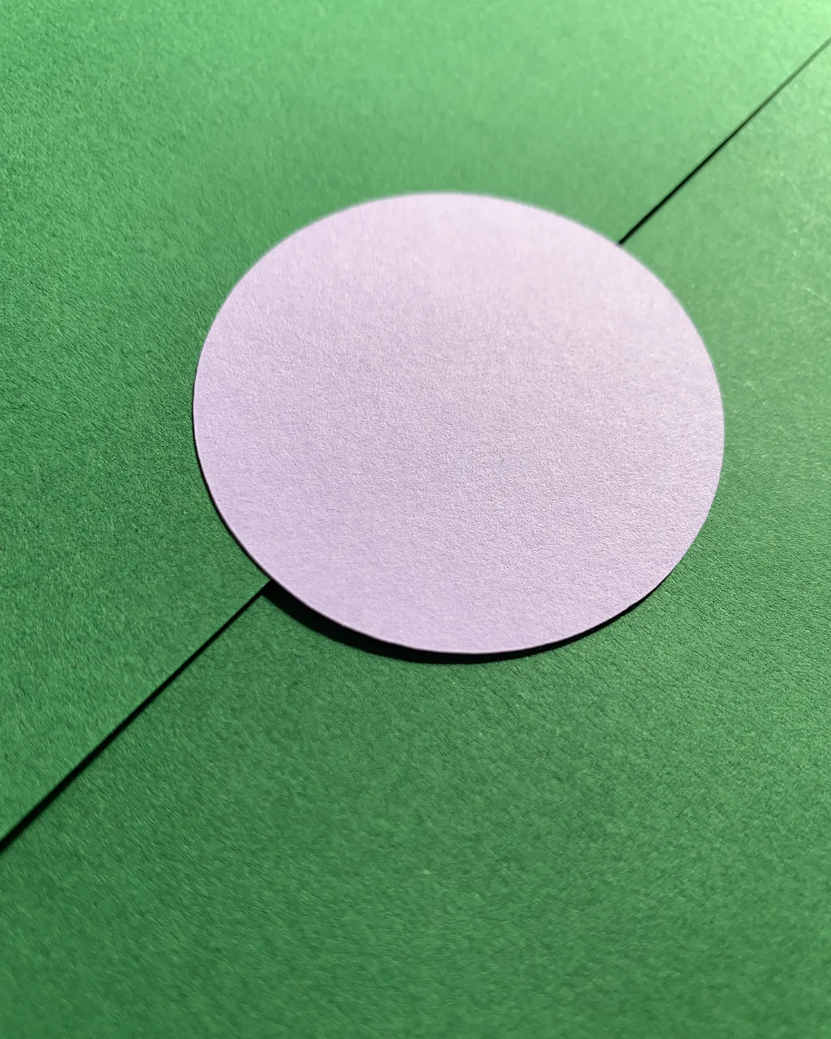 Close-up of a green paper envelope sealed with a round, blank light pink sticker.